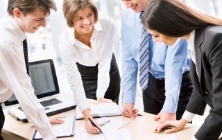 Four young people having a huddle around a desk.
